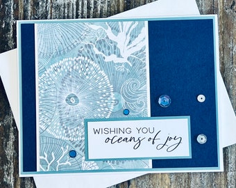 May include: A blue and white greeting card with the text "Wishing you oceans of joy" and blue and white sequins.