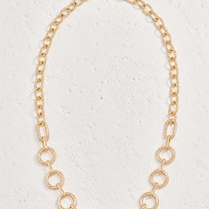 May include: A gold-toned necklace featuring a chain of elongated oval links at the top that transitions into a series of circular, interconnected rings along the bottom half. The piece includes a lobster claw clasp and an adjustable extender chain.