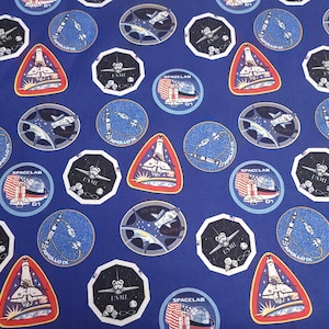 May include: Blue fabric with a repeating pattern of space shuttles, rockets, and stars. The fabric features the words "Space Lab" and "USML-1".
