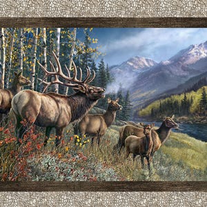 May include: A framed landscape painting depicts a herd of elk in a mountain setting. The elk, with their brown fur and large antlers, stand in a field of wildflowers. The background features a river, forest, and mountains under a cloudy sky.