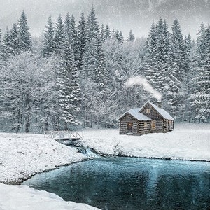 May include: A small wooden cabin with a snowy roof sits in a snowy forest. Smoke rises from the chimney. A small stream flows through the snow and into a frozen lake.