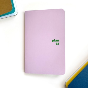 May include: A lavender-coloured notebook with the text "plan 52" printed in green.