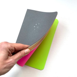 May include: A black notebook with a circle of dots and the letter "A" in the centre. The notebook is open to reveal colourful pages and a bright green cover.