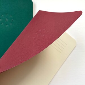 K&ouml;nnte beinhalten: Ein burgunderfarbenes Notizbuch mit cremefarbenem Innenleben und linierten Seiten. Der Einband hat ein dezentes Pr&auml;gemuster aus Punkten in einem Kreis.