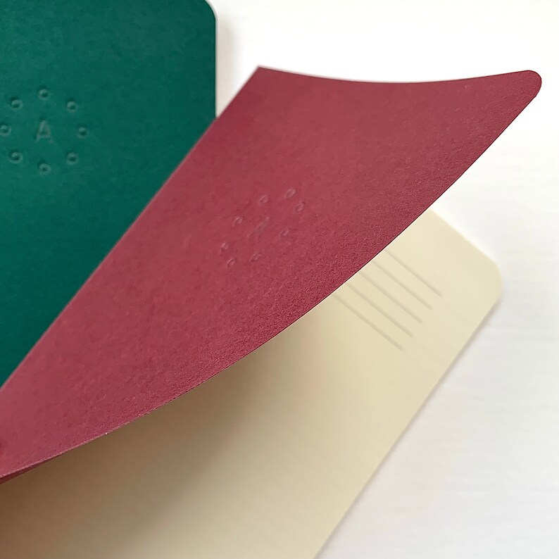 K&ouml;nnte beinhalten: Ein burgunderfarbenes Notizbuch mit cremefarbenem Innenleben und linierten Seiten. Der Einband hat ein dezentes Pr&auml;gemuster aus Punkten in einem Kreis.