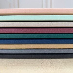 K&ouml;nnte beinhalten: Ein Stapel aus zehn verschiedenenfarbigen Kartonb&ouml;gen. Die Farben sind rosa, hellgr&uuml;n, beige, burgunderrot, dunkelgr&uuml;n, marineblau, braun, grau und schwarz.