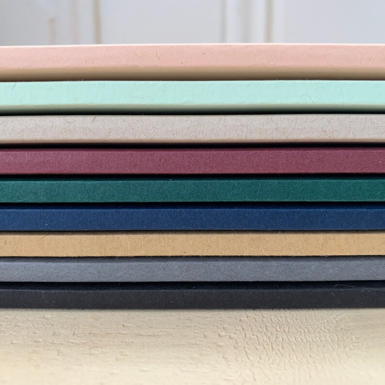 K&ouml;nnte beinhalten: Ein Stapel aus zehn verschiedenenfarbigen Kartonb&ouml;gen. Die Farben sind rosa, hellgr&uuml;n, beige, burgunderrot, dunkelgr&uuml;n, marineblau, braun, grau und schwarz.