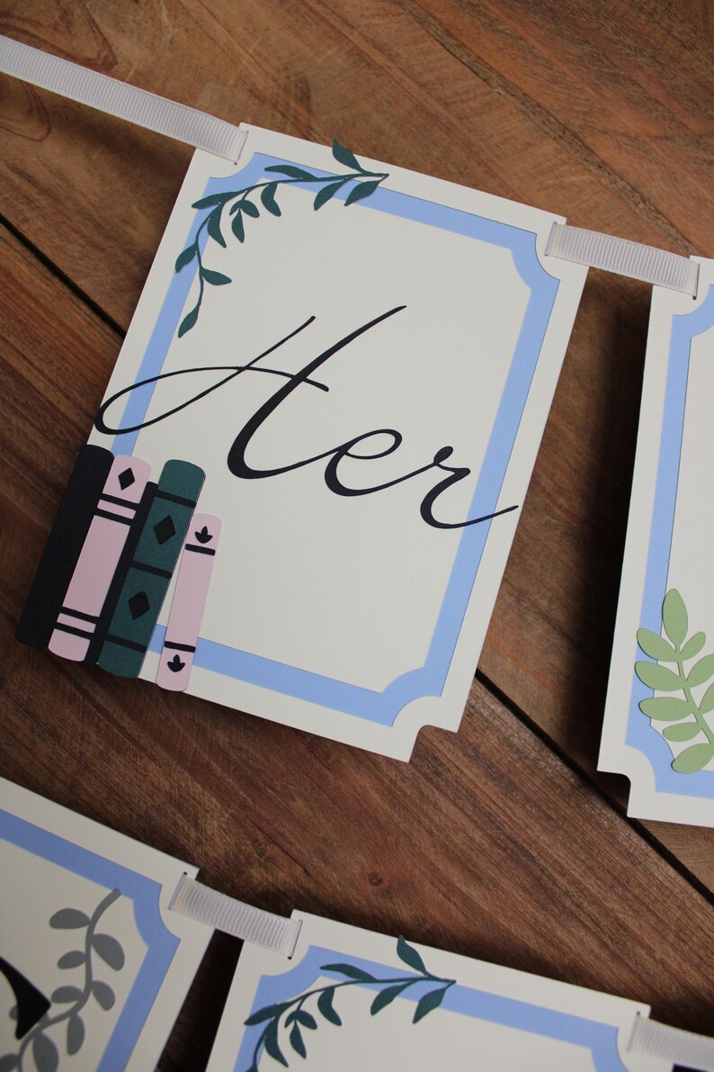May include: A banner with the word "Her" in elegant script, framed by a light blue border and decorative leaves. The banner includes illustrations of books in pink, green, and black. The banner is strung with a white ribbon.