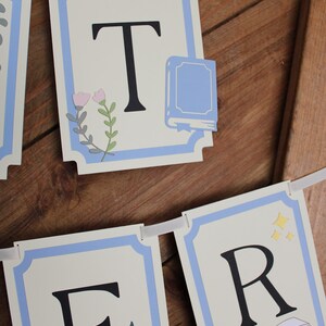 May include: A banner with individual lettered cards spelling out "TER". Each card has a light blue border and a white background. The letters are black. Some cards have floral and book illustrations.