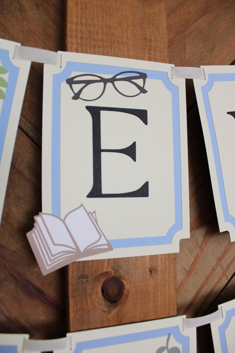 May include: A banner with a light blue border and a cream-colored background. The banner features a large black letter "E", a pair of glasses, and a small open book. The banner is strung with a white ribbon.