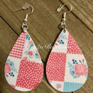 May include: A pair of teardrop-shaped earrings with a patchwork design. The earrings feature a pattern of pink and white gingham, floral, and blue accents. The text "Stacy Lee Rainbows" is visible on the earrings.