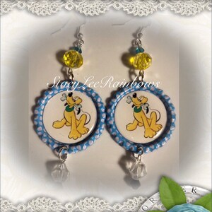 May include: A pair of dangle earrings featuring a blue and white polka dot design with a cartoon image of Pluto the dog holding a bone. The earrings have a yellow crystal bead and a clear crystal dangle.