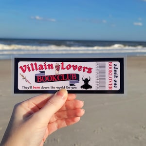 May include: A black and white ticket with red text that reads "Villain Lovers Bookclub" and "They'll burn down the world for you". The ticket also has a barcode and the text "admit one BOOKLOVER" on the right side.