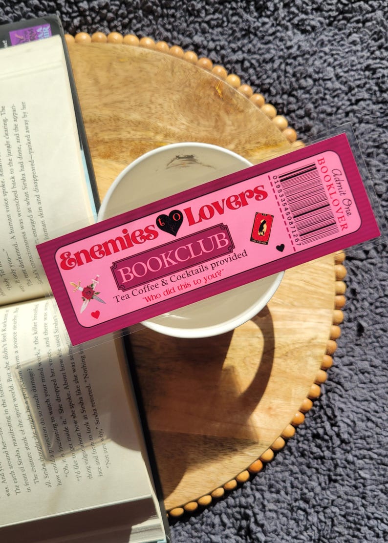 May include: Pink and black bookmark with the text "Enemies to Lovers Bookclub" and "Tea Coffee & Cocktails provided" with a small illustration of a rose and a dagger. The bookmark also has a barcode and the text "Admit One Booklover".
