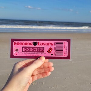 May include: A pink and red bookmark with the text "Enemies Lovers Bookclub" and the text "Tea Coffee & Cocktails provided" and "Who did this to you?"  The bookmark has a barcode and the text "Admit One BOOKLOVER".
