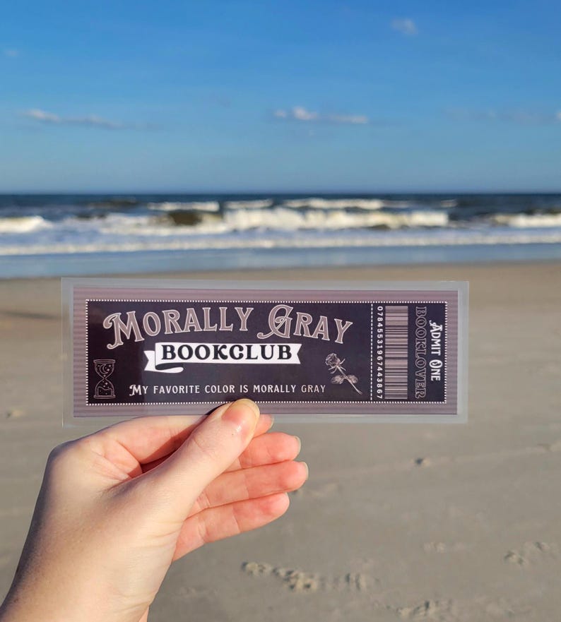 May include: A ticket for the "Morally Gray Bookclub" with the text "My favorite color is morally gray" and a rose illustration. The ticket is held in a hand against a beach background.