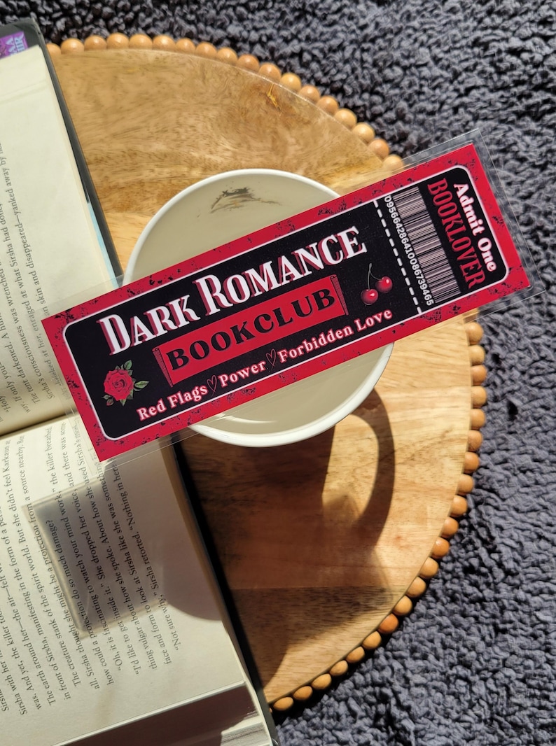May include: A red and black bookmark with the text "Dark Romance Bookclub" and "Red Flags Power Forbidden Love". The bookmark is shaped like a ticket with a cherry graphic and the text "Booklover" and "Admit One".
