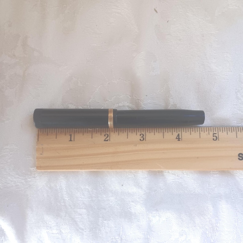 K&ouml;nnte beinhalten: Ein schwarzer F&uuml;llfederhalter mit goldenem Band, auf einem Holzlineal. Der Stift ist etwa 13 cm lang. Das Lineal ist in Zoll unterteilt.