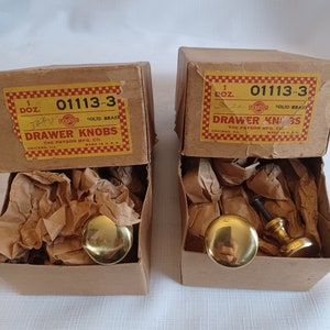 May include: Two boxes of solid brass drawer knobs. The boxes are labeled "DRAWER KNOBS" and "THE PAYSON MFG. CO." The knobs are gold-colored and have a rounded shape. The boxes are made in the U.S.A.