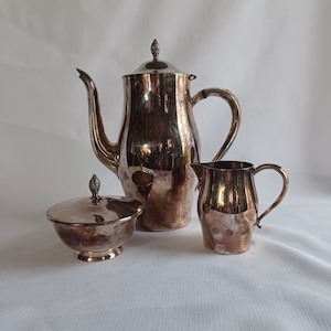 May include: A silver tea set with a teapot, creamer, and sugar bowl. The teapot has a decorative knob on the lid.