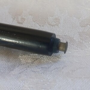 K&ouml;nnte beinhalten: Nahaufnahme eines schwarzen F&uuml;llfederhalters mit goldfarbenen Akzenten. Der Stift hat Text an der Seite und eine aufschraubbare Spitze. Der Stift liegt auf einer wei&szlig;en, strukturierten Oberfl&auml;che.