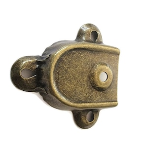 May include: Antique gold-toned metal latch with a rounded oval shape and three mounting holes. The latch has a worn, distressed finish.