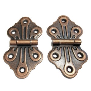 May include: Two antique-style copper hinges with a decorative design. The hinges are closed and have a dark brown patina.