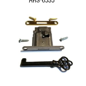 Peut inclure: Une serrure de cabinet argentée avec un trou de serrure et une clé noire. La serrure est montée sur une plaque argentée avec deux vis. La clé est ornée d'une tête décorative.