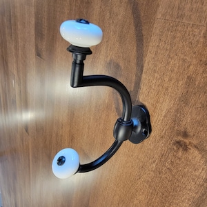 May include: Black metal coat hook with two white ceramic knobs.