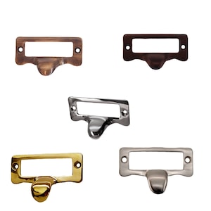 May include: Five drawer pulls in different finishes: brass, bronze, nickel, and pewter. Each pull has a rectangular label holder with rounded edges.