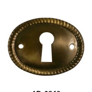May include: A brass keyhole cover with an oval shape and a rope-like border. The keyhole is in the center of the cover. The cover is labeled "AB-0249".
