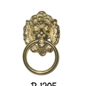 May include: A gold lion head door knocker with a ring pull. The knocker is a decorative piece with a detailed lion face and a circular ring pull. The text "B-1205" is printed below the knocker.