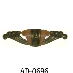 May include: Antique-style cabinet pull with a bronze finish and a central peach-colored accent. The pull features a stylized design with curved edges and a decorative center. The text "AD-0696" is printed below the pull.