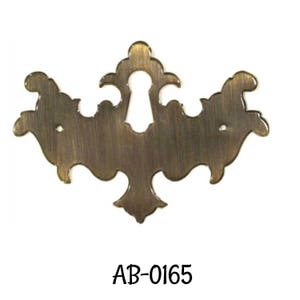May include: A brass keyhole cover with a decorative, ornate design. The cover has a keyhole cut-out in the center and a brushed finish. AB-0165
