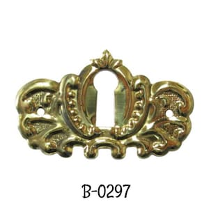 May include: A gold-toned metal keyhole cover with a decorative, ornate design. The cover has a keyhole in the center and a decorative border around the edge. The text "B-0297" is printed below the cover.