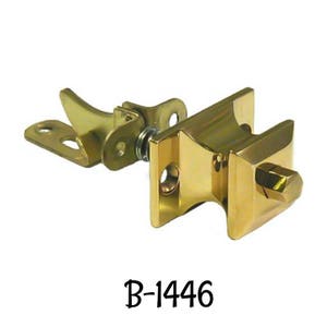 May include: A gold-toned door latch with a spring-loaded lever. The latch has a square shape and a rounded edge. The lever is attached to the latch with a metal arm. The latch is labeled "B-1446".