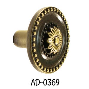 May include: A gold-toned metal knob with a decorative floral design in the center. The knob has a beaded edge and a short stem.