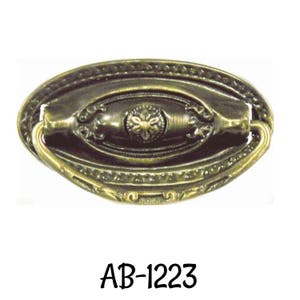 May include: An antique-style drawer pull with an oval shape and a decorative floral center. The pull has a bronze finish and features ornate detailing around the edges and handle. The text "AB-1223" is printed below the pull.