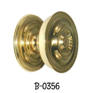 May include: A gold door knob with a white center and a decorative rim. The knob is labeled "B-0356".