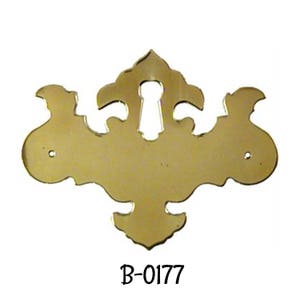 May include: A gold-toned metal keyhole cover with a decorative, ornate design. The cover has a keyhole cutout in the center and two small holes on either side. The cover is labeled "B-0177".