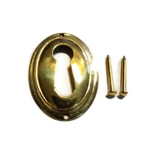 May include: A gold keyhole cover with a rounded oval shape and two small gold screws. The product number 1220-PB is printed below the keyhole cover.