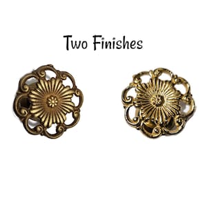 May include: Two ornate gold-toned metal drawer pulls with a floral design. The pulls are shown in two finishes, one with a more polished gold finish and the other with a more antique gold finish.