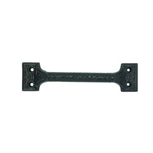 May include: Black cast iron door pull with an ornate design. The pull has two holes for mounting.