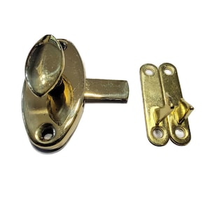 May include: A gold-toned door latch with a rounded oval-shaped base and a lever handle. The latch has a small, oval-shaped knob on the handle. The latch is designed to be mounted on a door and has a strike plate that is also gold-toned.