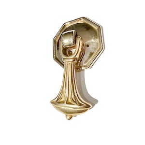 May include: A gold-toned cabinet pull with an octagonal base and a decorative, ornate, bell-shaped handle.