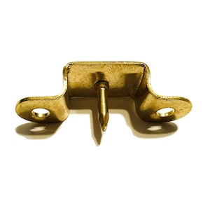 May include: A gold-toned metal hook with a pointed nail. The hook has two holes on each side and is designed to be attached to a wall or other surface.