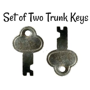 May include: Set of two silver-toned trunk keys. The keys have a rounded, oval-shaped head with a small hole in the center. The keys have a simple, functional design.
