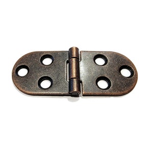 May include: A close-up of a  brass-colored hinge with four holes on each side. The hinge is closed and has a slightly oval shape.