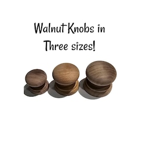 May include: Three wooden walnut knobs in varying sizes. The knobs have a rounded top and a circular base. The text "Walnut Knobs in Three sizes!" is displayed above the knobs.