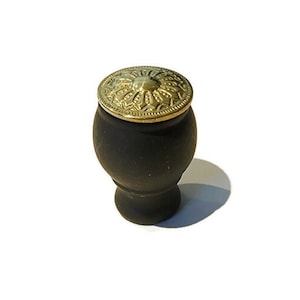 Peut inclure: Un récipient en bois noir avec un couvercle en métal doré orné d'un motif floral décoratif. Le couvercle est légèrement surélevé et a une forme arrondie.